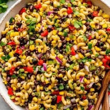 Vibrant Cowboy Caviar Pasta Salad for Easy Meals 3 A vibrant close-up of cowboy caviar pasta salad in a rustic ceramic bowl, featuring elbow macaroni, black beans, corn, red bell pepper, red onion, green onions, and fresh cilantro, served with wooden spoons.