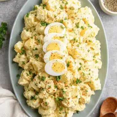 The Ultimate Creamy Southern Potato Salad 3 Creamy southern potato salad on a blue platter, garnished with paprika, fresh parsley, and hard-boiled egg halves.