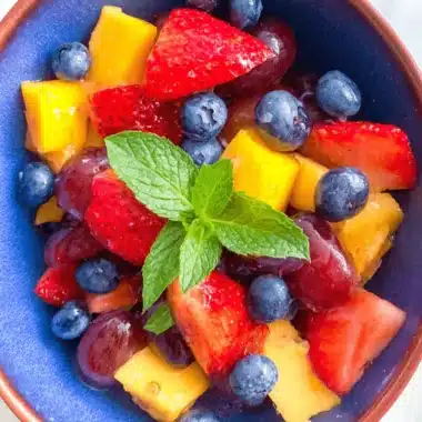 Ultimate Summer Fruit Salad with Mint 3 Vibrant summer fruit salad with mint in a rustic blue bowl, featuring mango, strawberries, grapes, and blueberries.