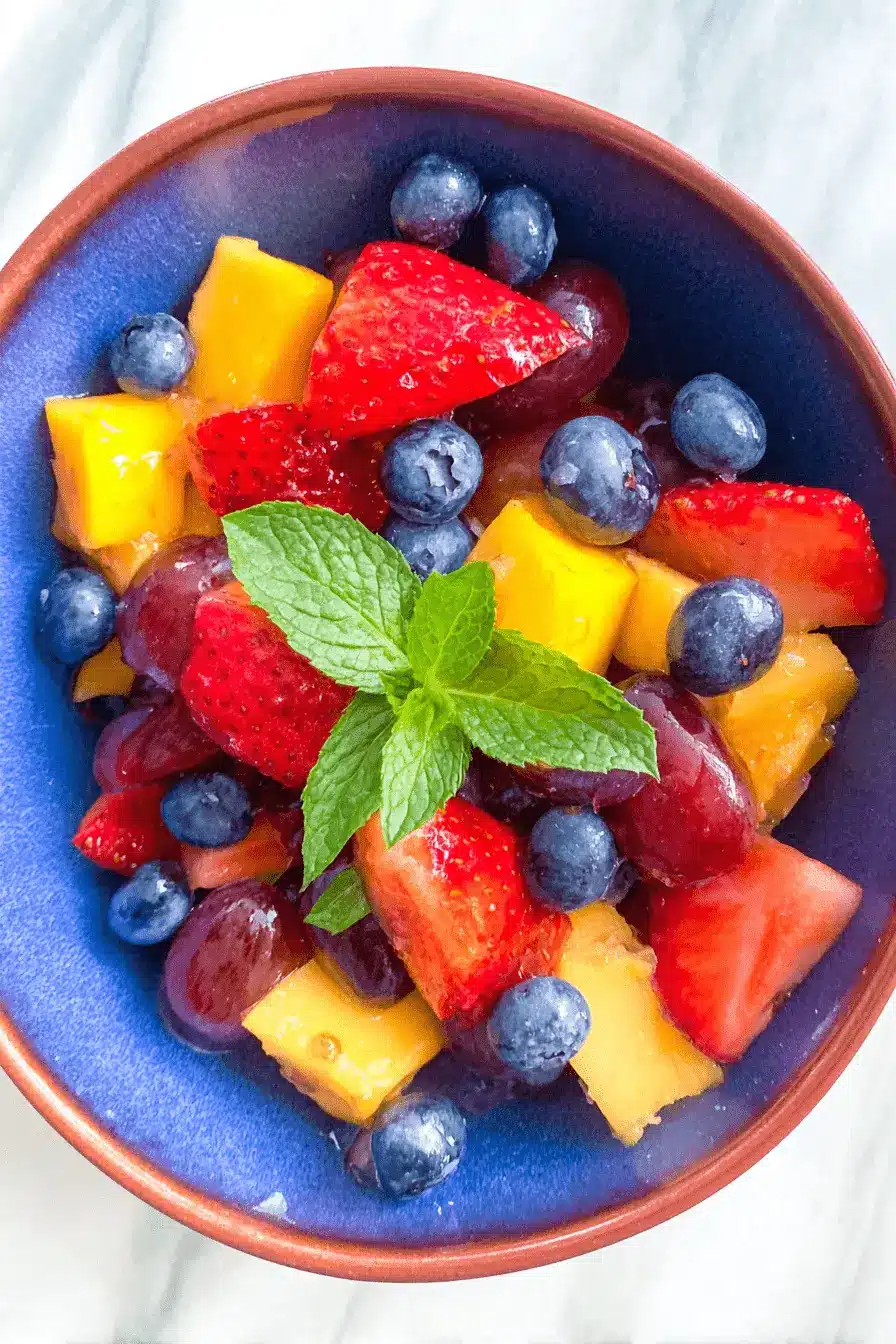 Ultimate Summer Fruit Salad with Mint 2 Vibrant summer fruit salad with mint in a rustic blue bowl, featuring mango, strawberries, grapes, and blueberries.