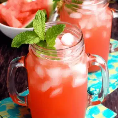 Quick & Easy Watermelon Cooler Recipe 3 Close-up of two refreshing watermelon coolers in mason jars, garnished with mint, on colorful checkered napkins.