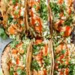 Amazing Bang Bang Shrimp Tacos 6 Six delicious bang bang shrimp tacos, topped with cabbage, seasoned shrimp, creamy sauce, cilantro, and a spicy red drizzle, arranged on a light gray surface.