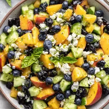 Vibrant Blueberry Peach Feta Salad Recipe 4 Close-up overhead shot of a vibrant blueberry peach feta salad in a rustic gray bowl with fresh herbs and a light vinaigrette.