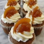 Amazing Peach Cobbler Cupcakes Recipe 6 Close-up of delicious peach cobbler cupcakes with creamy frosting and fresh peach slices on a marble surface.