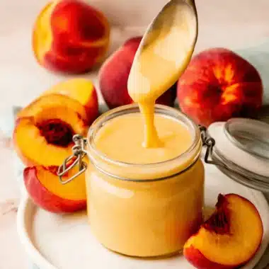 Simple & Luxurious Homemade Peach Curd 3 Close-up of creamy peach curd in a glass jar with fresh peaches and an antique spoon.