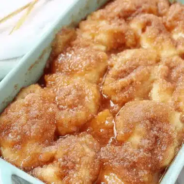 Magic Peach Dumplings: Quick & Easy Dessert 3 Close-up of golden baked peach dumplings in a turquoise baking dish, dusted with cinnamon-sugar.