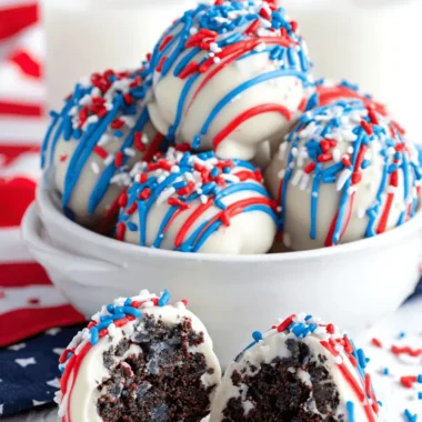 Amazing Foolproof Patriotic Oreo Balls 3 Delightful Patriotic Oreo Balls, spherical and coated in white chocolate with red, white, and blue drizzles and sprinkles, revealing a dark chocolate interior, served with milk.