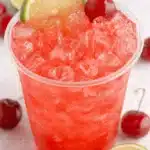Vibrant Fresh Cherry Limeade Recipe 6 Close-up of a vibrant fresh cherry limeade, garnished with a lime slice and a ripe cherry, served in a clear plastic cup.