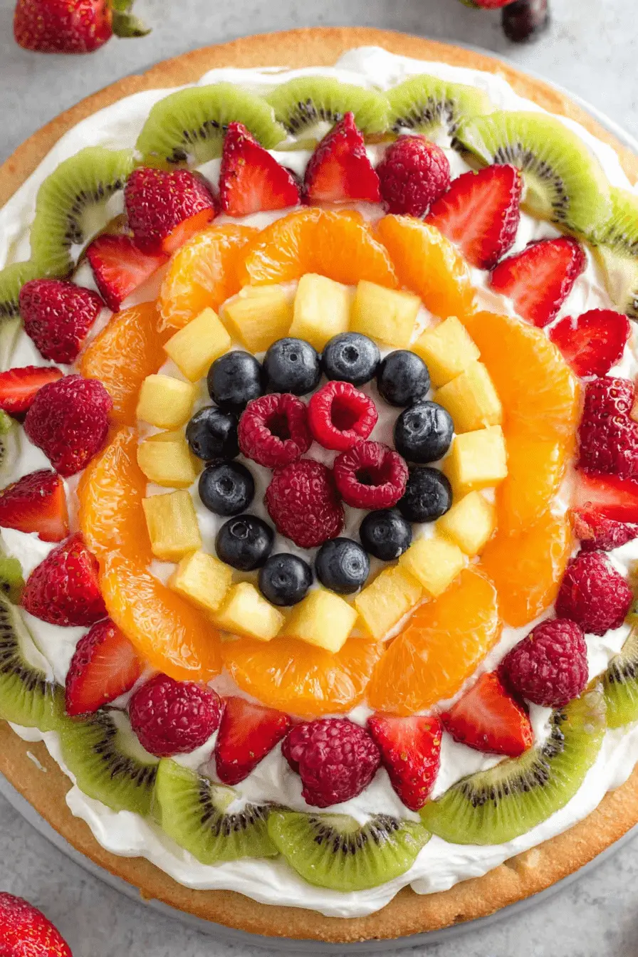 Stunning Fruit Pizza: Easy Summer Dessert 2 Overhead shot of a vibrant fruit pizza featuring a golden crust and a colorful array of fresh kiwi, strawberries, oranges, pineapple, blueberries, and raspberries.