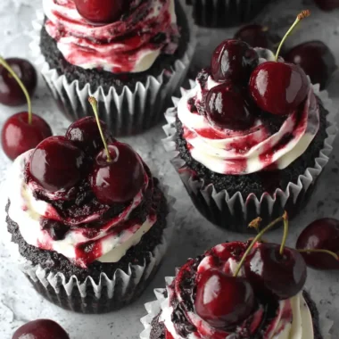 Simple Chocolate Cherry Cupcakes Recipe 3 Four decadent chocolate cherry cupcakes with white frosting, cherry compote, and fresh cherries on a stone surface.