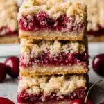 Amazing Cherry Crumble Bars: Easy & Foolproof 7 Close-up of stacked cherry crumble bars with a golden-brown base, vibrant cherry filling, and crumbly topping, surrounded by fresh cherries.