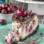 The Ultimate Foolproof Chocolate Cherry Cheesecake 8 Decadent slice of chocolate cherry cheesecake on a floral plate with ganache and fresh cherries.