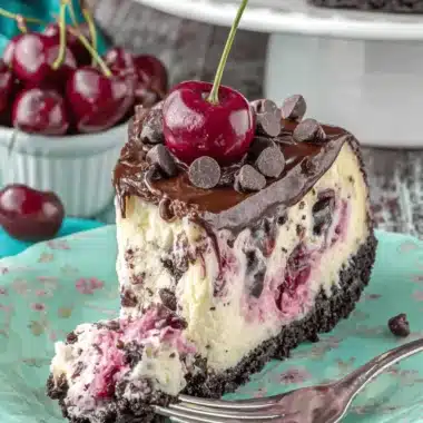 The Ultimate Foolproof Chocolate Cherry Cheesecake 3 Decadent slice of chocolate cherry cheesecake on a floral plate with ganache and fresh cherries.