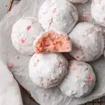 Easy & Irresistible Cherry Almond Snowball Cookies 7 Close-up of powdered sugar-dusted Cherry Almond Snowball Cookies on a wire rack, revealing their pale pink interior and red specks.