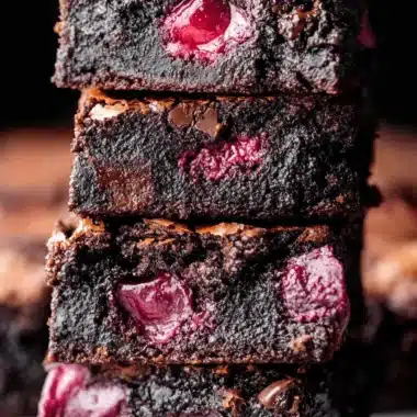 Ultimate Fudgy Cherry Brownies 3 Close-up of a stack of rich, fudgy dark chocolate cherry brownies, showcasing vibrant red cherries and a slightly cracked top.