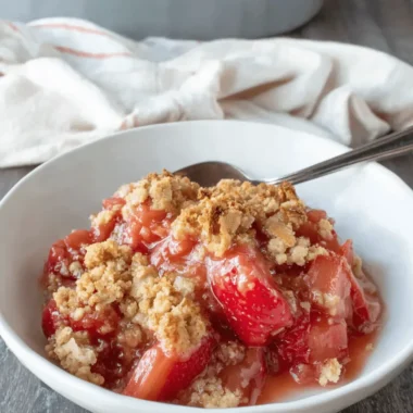 Amazing Rhubarb Crisp: A Foolproof Recipe 3 Close-up of a delicious strawberry rhubarb crisp in a white bowl with a golden streusel topping, ready to eat on a rustic wooden background.