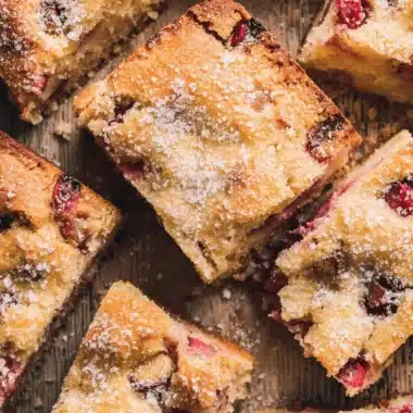 The Ultimate Foolproof Rhubarb Cake 4 Close-up of rustic rhubarb cake slices dusted with powdered sugar on a wooden surface.