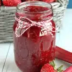 Amazing Strawberry Rhubarb Jam: Simple Guide 6 Homemade strawberry rhubarb jam in a mason jar, surrounded by fresh strawberries and rhubarb stalks on a rustic wooden surface.