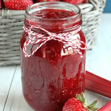 Amazing Strawberry Rhubarb Jam: Simple Guide 4 Homemade strawberry rhubarb jam in a mason jar, surrounded by fresh strawberries and rhubarb stalks on a rustic wooden surface.