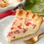 Ultimate Foolproof Rhubarb Custard Pie 9 A delicious slice of homemade rhubarb custard pie on a floral plate, with fresh rhubarb in the background.