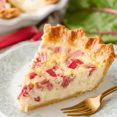 Ultimate Foolproof Rhubarb Custard Pie 3 A delicious slice of homemade rhubarb custard pie on a floral plate, with fresh rhubarb in the background.