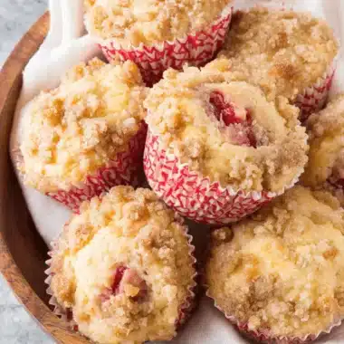 Irresistibly Moist Strawberry Rhubarb Muffins 3 A close-up of freshly baked strawberry rhubarb muffins with a golden-brown streusel topping nestled in a wooden bowl.