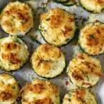 Amazing Baked Zucchini: Your New Favorite Side 5 Close-up of golden-brown cheesy baked zucchini rounds on parchment paper, garnished with fresh herbs.