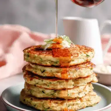 Ultimate Crispy Zucchini Pancakes 3 Stack of golden-brown zucchini pancakes with syrup being poured, garnished with cream and green onions.