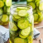 Amazing Refrigerator Pickles: Easy & Crispy! 15 Close-up of a mason jar filled with fresh, thinly sliced cucumber refrigerator pickles in brine, adorned with spices on a wooden surface.