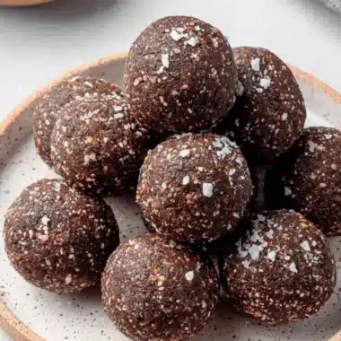 Amazing 10-Minute Fig Energy Balls 3 Close-up of homemade fig energy balls sprinkled with sea salt on a ceramic plate, with dried figs in the background.