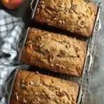 Amazing Moist Peach Bread Recipe 7 Close-up of three freshly baked peach bread loaves with walnuts cooling on a wire rack, next to fresh peaches.