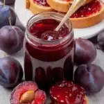 Wonderful Foolproof No-Pectin Plum Jam 5 Close-up of homemade plum jam in a glass jar, surrounded by fresh dark purple plums and toasted bread spread with glistening plum jam.