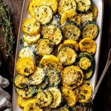 Amazing Foolproof Roasted Zucchini & Yellow Squash 3 Top-down view of a white platter filled with perfectly roasted zucchini and yellow squash, garnished with Parmesan and fresh herbs.