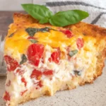 The Ultimate Southern Tomato Pie Recipe 13 A close-up of a triangular slice of a delicious southern tomato pie recipe with golden crust, melted cheese, and fresh basil on a speckled plate.