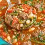 The Ultimate Hatch Green Chili Stew Recipe 9 Ladle serving hearty hatch green chili stew with beef, white beans, green beans, and tomatoes from a teal pot.