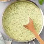 Quick Creamy Pesto Sauce: Your Weeknight Hero 7 Top-down view of creamy pesto sauce being stirred in a stainless steel pan, with penne pasta and fresh basil.