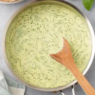 Quick Creamy Pesto Sauce: Your Weeknight Hero 4 Top-down view of creamy pesto sauce being stirred in a stainless steel pan, with penne pasta and fresh basil.