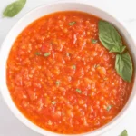 The Ultimate Cherry Tomato Sauce Recipe 5 Close-up of a vibrant, chunky cherry tomato sauce in a light bowl, garnished with fresh basil.