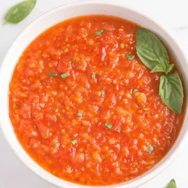 The Ultimate Cherry Tomato Sauce Recipe 4 Close-up of a vibrant, chunky cherry tomato sauce in a light bowl, garnished with fresh basil.
