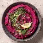Vibrant Beet Hummus: Easy & Ultra-Creamy Dip 6 Vibrant pink beet hummus swirled in a grey bowl, garnished with fresh herbs and a lemon slice.