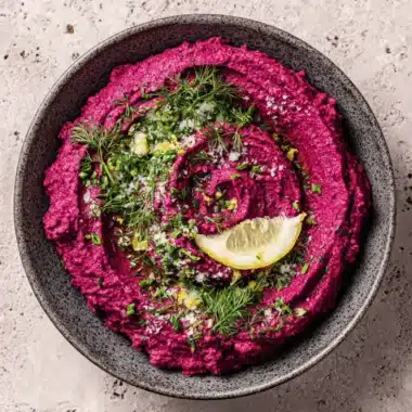 Vibrant Beet Hummus: Easy & Ultra-Creamy Dip 4 Vibrant pink beet hummus swirled in a grey bowl, garnished with fresh herbs and a lemon slice.