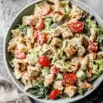 Amazing Ceasar Pasta Chicken Salad: Quick Dinner 6 Top-down view of a vibrant ceasar pasta chicken salad in a light blue ceramic bowl, featuring grilled chicken, farfalle pasta, cherry tomatoes, and fresh greens.