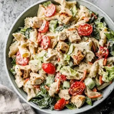 Amazing Ceasar Pasta Chicken Salad: Quick Dinner 3 Top-down view of a vibrant ceasar pasta chicken salad in a light blue ceramic bowl, featuring grilled chicken, farfalle pasta, cherry tomatoes, and fresh greens.