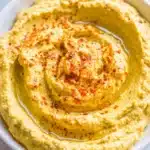 Unparalleled: How to Make Hummus Creamy & Smooth 5 Creamy homemade hummus in a white bowl with olive oil and spices, illustrating how to make hummus.