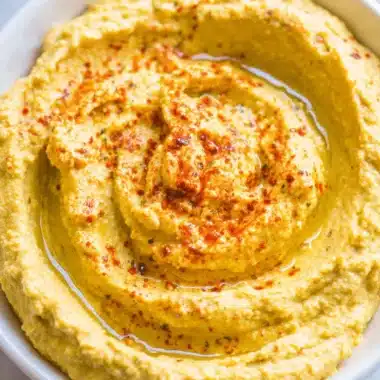 Unparalleled: How to Make Hummus Creamy & Smooth 4 Creamy homemade hummus in a white bowl with olive oil and spices, illustrating how to make hummus.