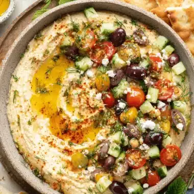 Stunning Loaded Hummus: Easy, Impressive & Delicious 3 Top-down view of a rustic bowl of loaded hummus, garnished with olive oil, paprika, fresh dill, diced tomatoes, cucumber, Kalamata olives, feta cheese, and whole chickpeas, served with toasted pita bread.