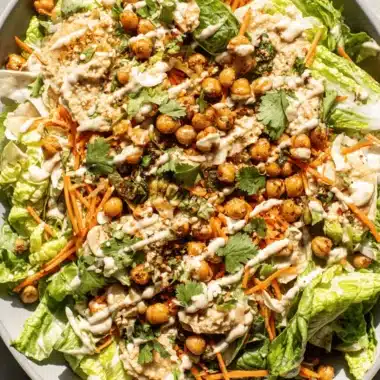 Amazing Hummus Salad: Quick & Creamy Recipe 4 Vibrant hummus salad with fresh greens, roasted chickpeas, and tahini drizzle in a light gray bowl.