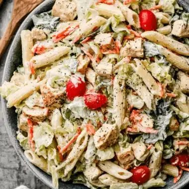 Amazing Ceasar Pasta Chicken Salad 4 Close-up overhead view of a vibrant ceasar pasta chicken salad with penne, grilled chicken, and fresh vegetables in a rustic grey bowl.