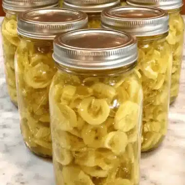 The Ultimate Guide to Canning Banana Peppers 3 Glass jars of home-canned sliced bananas on a marble surface, showcasing the preservation process, also applicable to canning banana peppers.