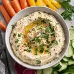 Ultimate 5-Minute Creamy White Bean Hummus 5 Close-up of creamy white bean hummus garnished with olive oil, parsley, and paprika, served with fresh vegetables.